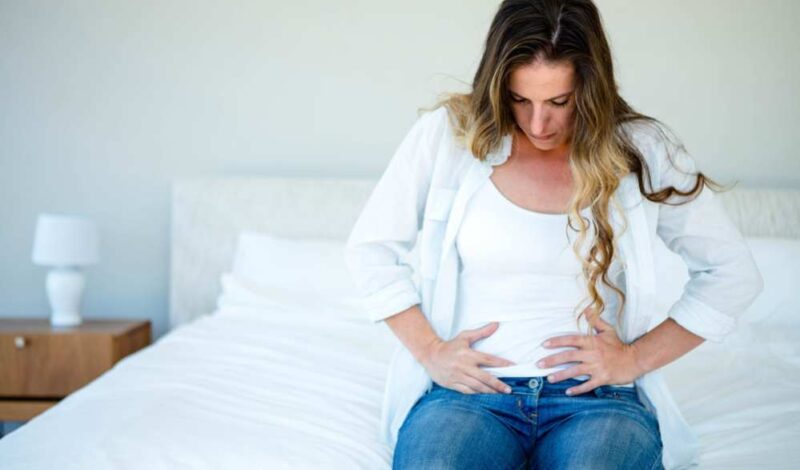woman sitting on her bed holding her stomach in discomfort