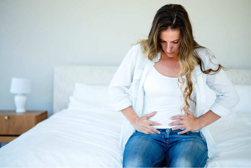 woman sitting on her bed holding her stomach in discomfort
