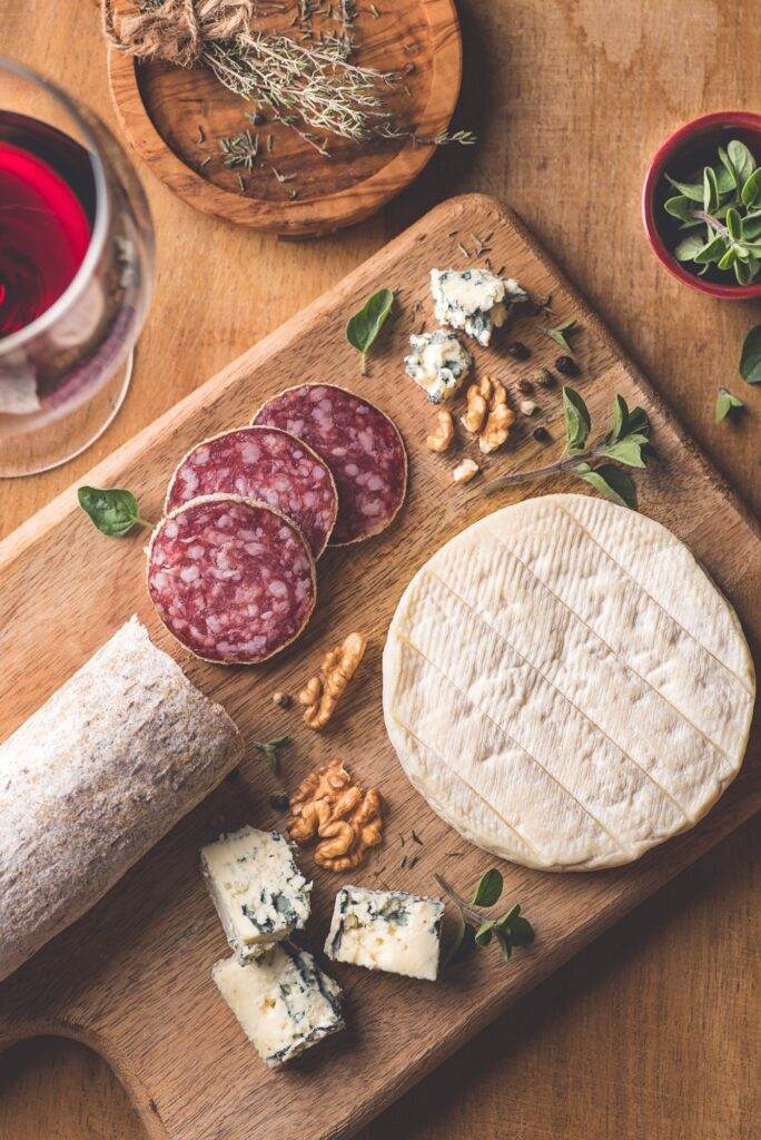 Histaminreiche Lebensmittel wie Rotwein, gereifter Käse und Wurst als auch Nüsse auf Holzbrett , italienisch mit Salbei gerichtet